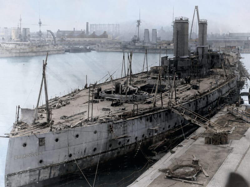 HMS Dreadnought fitting out at Portsmouth in 1906 - her name on the stern, her turret rings still empty, and the dockyard cranes at work over her deck