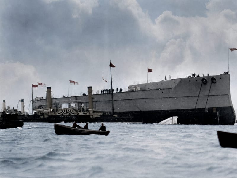 The bare hull of HMS Dreadnought afloat shortly after her launch at Portsmouth in February 1906, dressed with flags and attended by a paddle tug and small boats